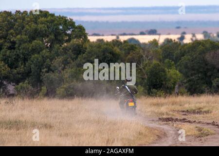 African-American ranger riding a patrol motorcycle near a tree forest in Kenya Stock Photo