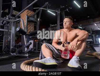 Tired man sits on a floor after hardworking in gym drinking water. Healthy lifestylel concept Stock Photo