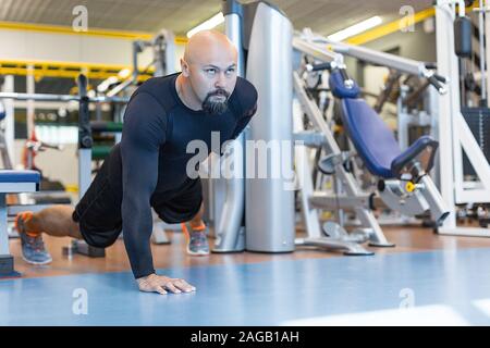 Brutal bearded man doing push ups exercise with one hand in fitness gym. Healty lifestyle concept Stock Photo