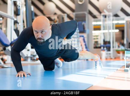 Brutal bearded man doing push ups exercise with one hand in fitness gym. Close up portrait. Healty lifestyle concept Stock Photo