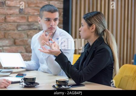 Two young male and female multiracial business people working connected with technological devices at the bar. Two young creative coworkers working wi Stock Photo