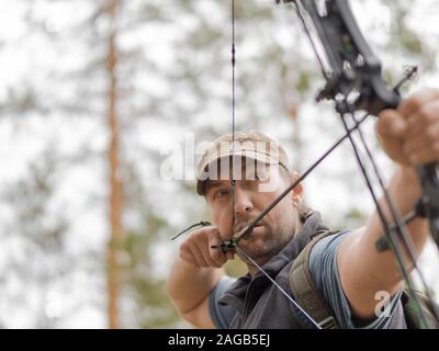 Man hunts in the forest with a bow. The hunter aims Stock Photo