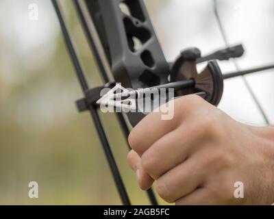 Close-up of a male hand holding a bow and a sharp arrowhead. Bow hunting in the forest. Focus on sharp arrowhead. Stock Photo