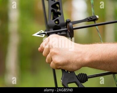 Bow hunting in the forest. Close-up hand holding a bow and an arrowhead Stock Photo