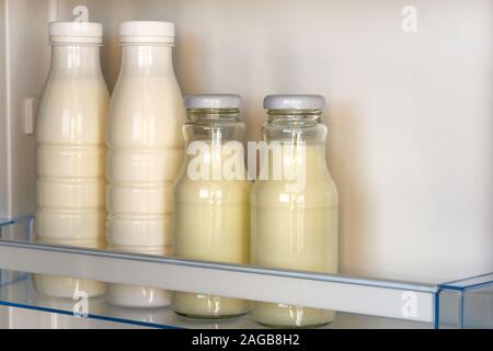 Dairy products in glass and plastic bottles on shelf of open empty fridge. White milk in refrigerator. Horizontal view. Stock Photo