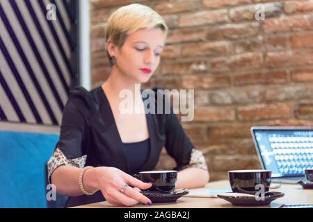 Young female business woman drinking coffee and  working connected with technological devices at the bar.  Young female creative coworker working with Stock Photo
