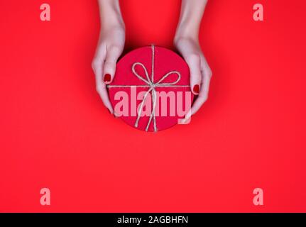 Closed red round gift box on red background. the view from the top. Gift for the holidays of New Year, Christmas, Valentine's day, March 8. Stock Photo