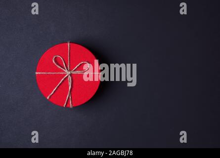 Closed red round gift box on black background. the view from the top. Gift for the holidays of New Year, Christmas, Valentine's day, March 8. Stock Photo