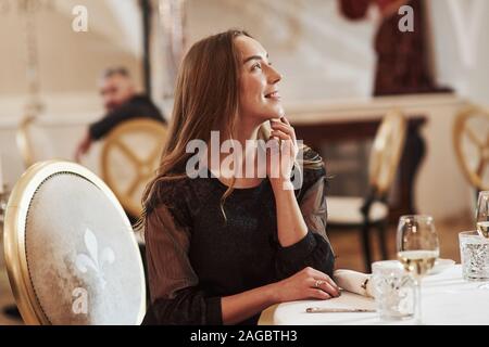 Smiling blonde sits on the golden colored chair in the luxury restaurant Stock Photo