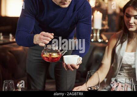 Man poring tea in white cup. Family friends having nice time in beautiful luxury modern restaurant