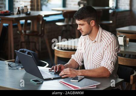 Busy with affairs. Adult man sits in cafe at daytime and using the laptop for the remote work