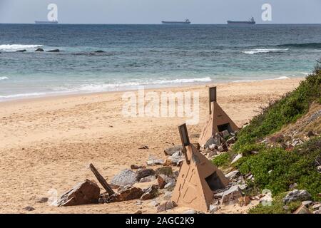 Newcastle, Australia - December 10, 2009: Sandy beach with beige concrete anchor cones and 3 large bulk ships waiting on blue-azure South Pacific Ocea Stock Photo