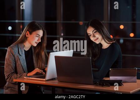 Laptops and tablet on the table. Team of young business people works on their project at night time in the office Stock Photo