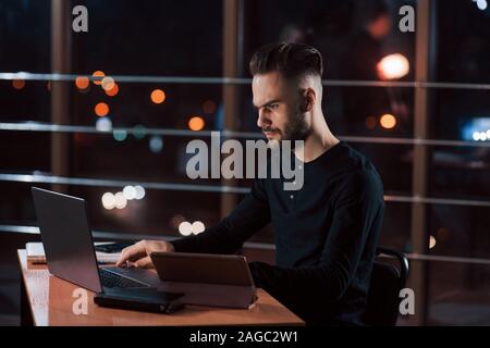 Side view. Stylish young businessman works alone in the office at nightime Stock Photo