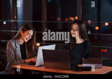 Together at the same table. Team of young business people works on their project at night time in the office Stock Photo