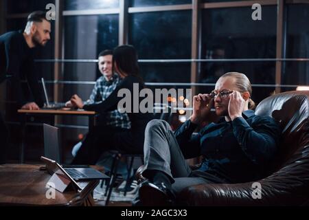 Wearing the glasses. Team of young business people works on their project at night time in the office Stock Photo