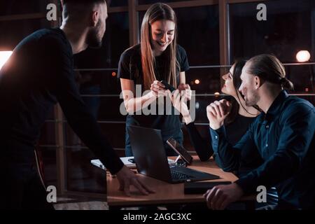 Having free time. Team of young business people works on their project at night time in the office Stock Photo