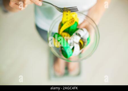 Diet and Weight Loss. Woman holds bowl and fork with measuring tape Stock Photo