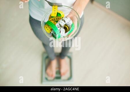 Diet and Weight Loss. Woman holds bowl and fork with measuring tape Stock Photo