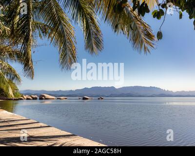 View of Catimbaú Beach, with coconut palm leaves and mountains in the background, Paqueta, Rio de Janeiro, Brazil Stock Photo