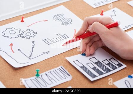 cropped view of woman holding red felt-tip pen near work notes on cork board Stock Photo