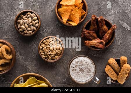 top view of bowls with nuts, crisps, chicken wings and fried cheese near mug of beer on brown surface Stock Photo