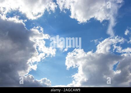 Beautiful blue sky with white clouds of an unusual shape. Clear summer sky with puffy cumulus clouds, heavenly landscape with sunbeams. Background wal Stock Photo
