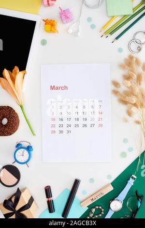 march calendar page, digital tablet, lily flower, spikelets, cosmetics, donut, pencils, gift boxes, wristwatch, toy alarm clock, block with march insc Stock Photo