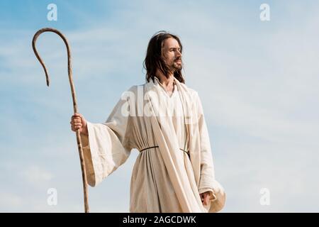 bearded man holding wooden cane against blue sky and clouds Stock Photo