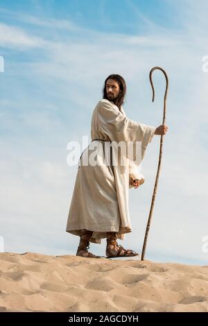 bearded man walking with wooden cane in desert Stock Photo