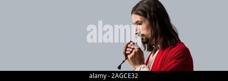 panoramic shot of religious man holding rosary beads while praying isolated on grey Stock Photo