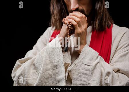 cropped view of man holding rosary beads while praying isolated on black Stock Photo