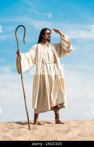 handsome bearded man holding wooden cane in desert Stock Photo