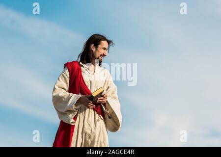 jesus holding cross and holy bible against sky with clouds Stock Photo