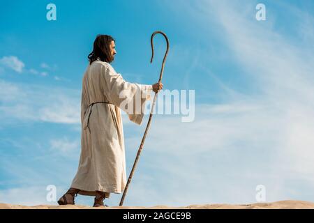 handsome bearded man holding wooden cane and walking in desert Stock Photo