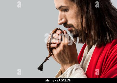 side view of man praying and holding rosary beads isolated on grey Stock Photo