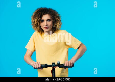 curly teenager riding electric scooter isolated on blue Stock Photo