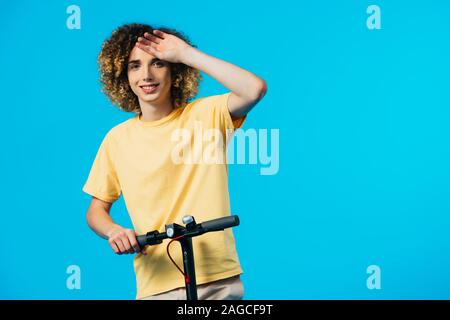 happy curly teenager riding electric scooter isolated on blue Stock Photo