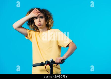 tired curly teenager riding electric scooter isolated on blue Stock Photo