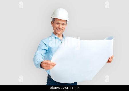 Construction. Mature man in hardhat standing isolated on white with blueprint smiling happy Stock Photo