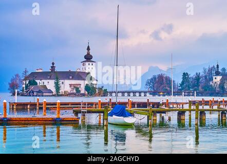 The running rainy clouds above the Traunsee lake with lonely sail yacht, moored in port and historical Schloss Ort on background, Gmunden, Salzkammerg Stock Photo