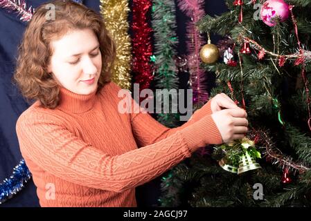 A girl decorates a Christmas tree with green bells. Christmas tree decorated with tinsel and toys. Bright manicure on fingernails. Stock Photo