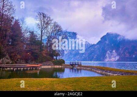 The pleasant evening walk along the Badeinsel recreational zone with a view on ripples on Traunsee lake and clouds, hovering the Traunstein mountain, Stock Photo