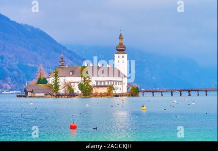 The heavy rainy clouds and grey mist covers the Alpine mountain range behind the outstanding Schloss Ort castle, located on the tiny islet amid the Tr Stock Photo