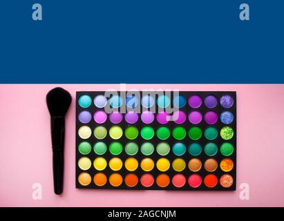Pallet of eyeshadows with a brush on bright pink and blue background with text. Stock Photo
