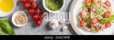 top view of cooked Pappardelle with tomatoes, basil and prosciutto near ingredients on grey surface, panoramic shot Stock Photo