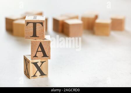 Three wooden cubes with word TAX on white table, more in background, space for text in right down corner Stock Photo
