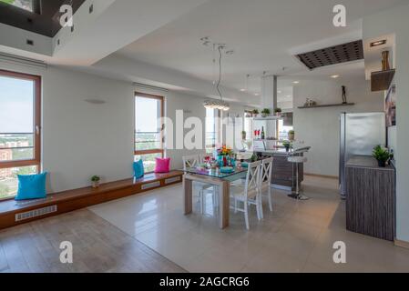 Kitchen in spacious modern studio apartment. Interior in light tones. View from window. Laid table. Kitchen set. Stock Photo