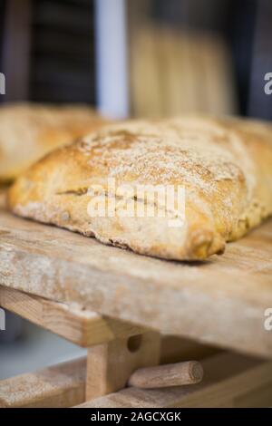 Vertical shot of freshly baked sourdough bread covered with flour on a wooden shelf Stock Photo