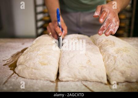 Professional chief cutting the dough into pieces for making delicious pizza Stock Photo